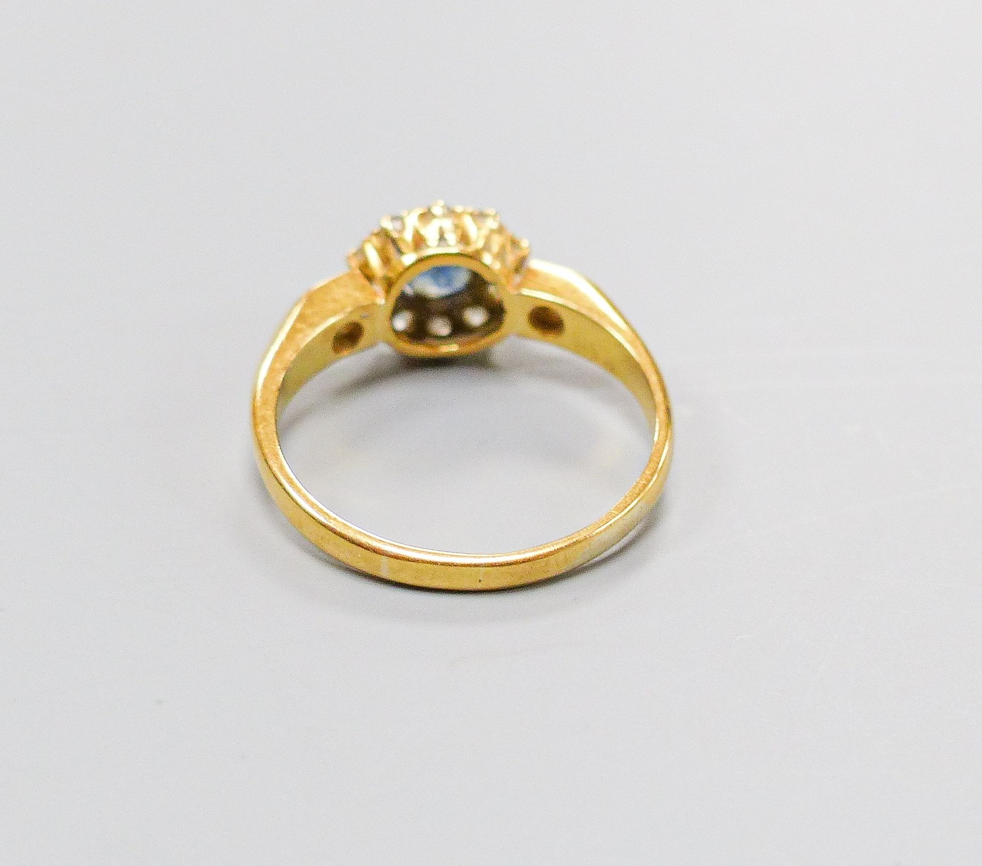 An 18ct, sapphire and diamond set circular cluster ring, with diamond set shoulders, size M, gross 3.4 grams.
